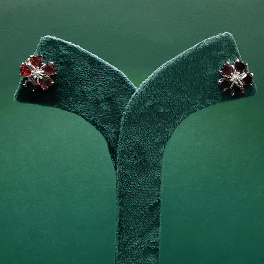 Pair of red and silver earrings on a green velvet stand against a green background