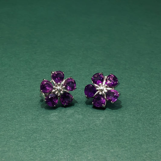 Pair of purple flower-shaped earrings on a green background