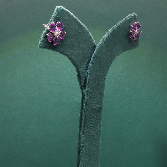 Purple gemstone earrings on a green stand against a green background