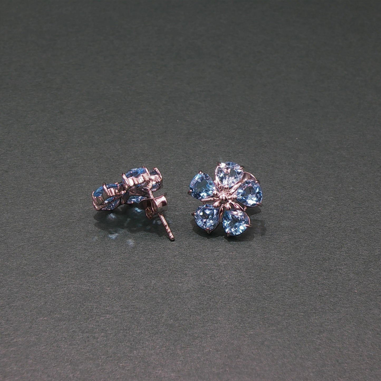 Pair of flower-shaped earrings with blue gemstones on a gray background

