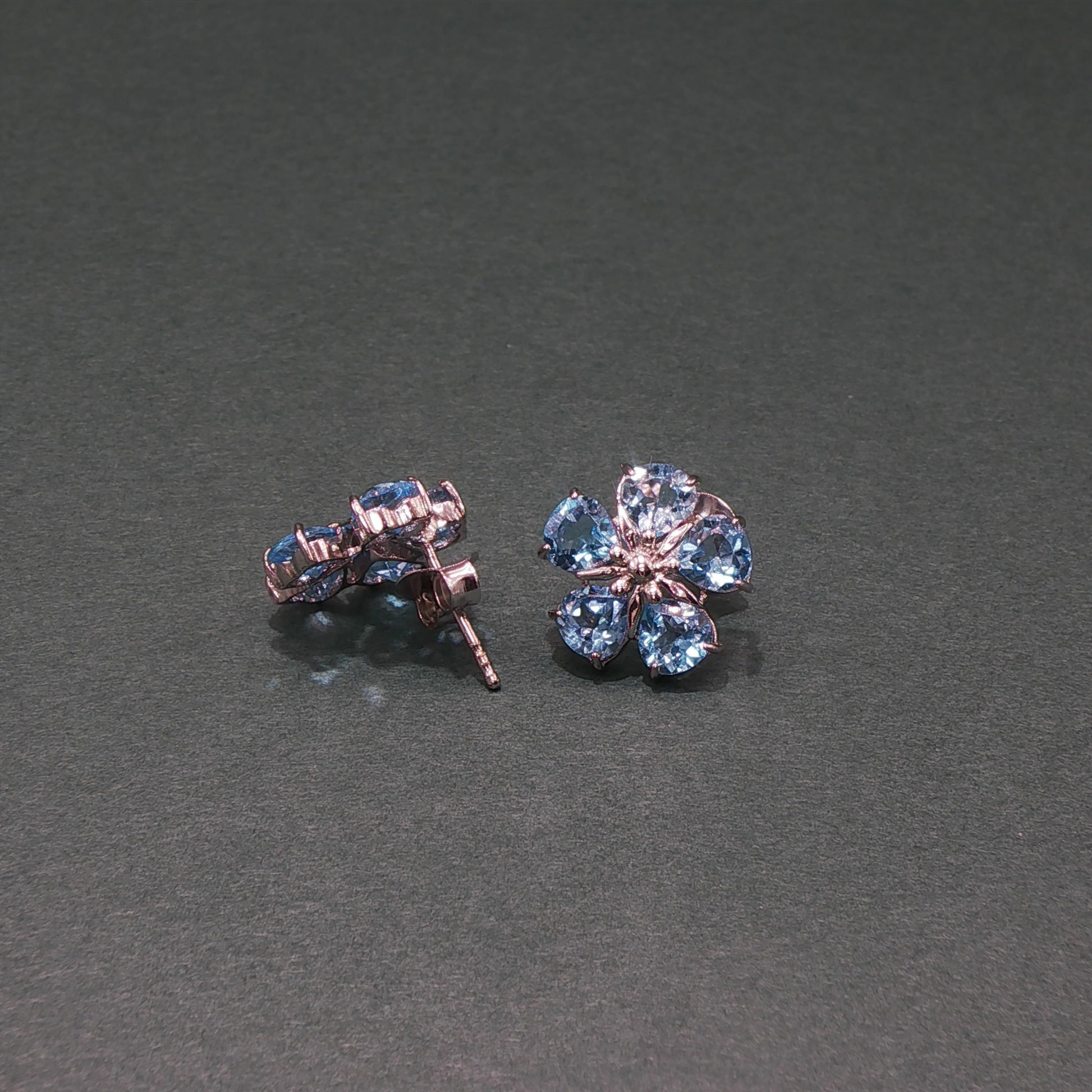 Pair of flower-shaped earrings with blue gemstones on a gray background
