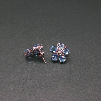 Pair of flower-shaped earrings with blue gemstones on a gray background
