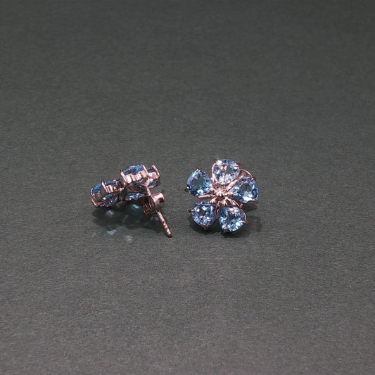 Pair of flower-shaped earrings with blue gemstones on a gray background
