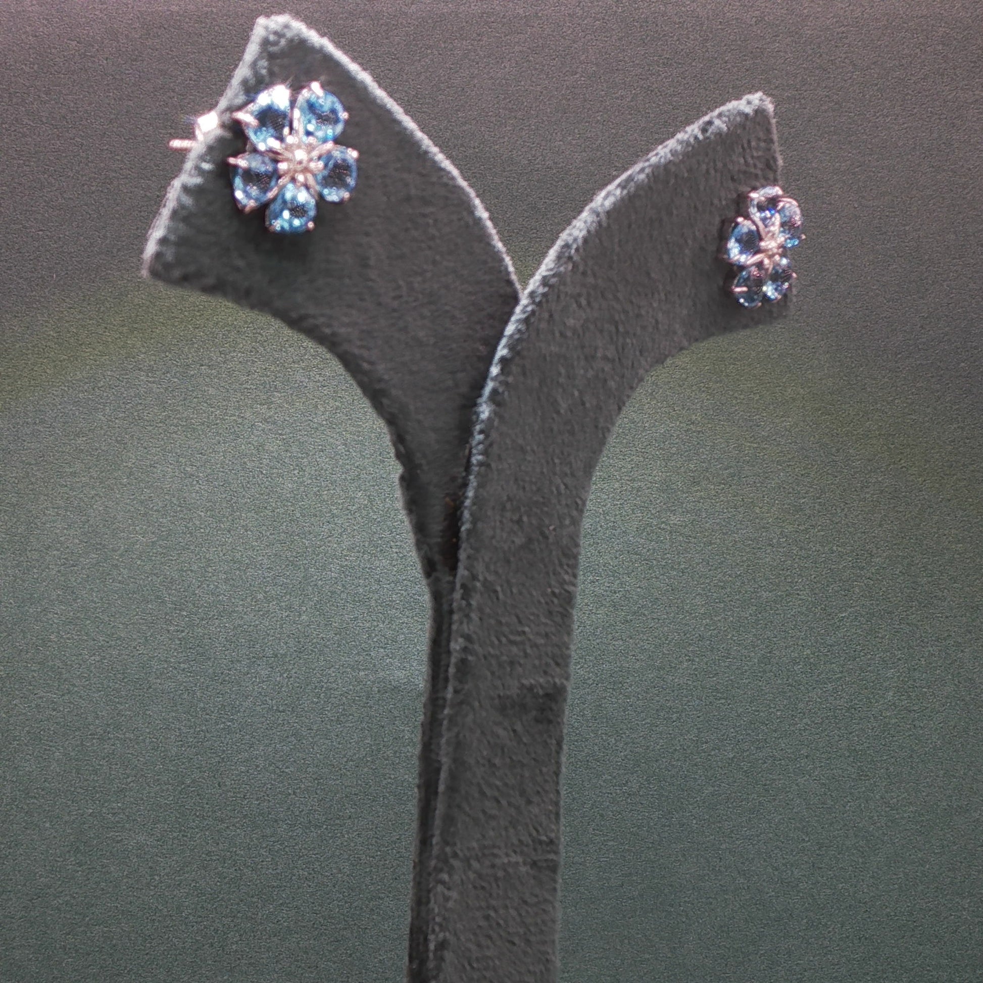 Pair of earrings on a grey stand against a dark background