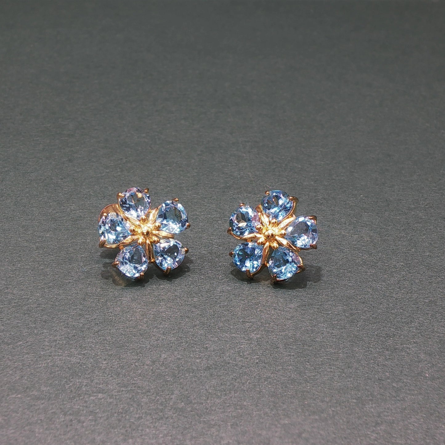 Pair of flower-shaped earrings with blue gemstones on a gray background