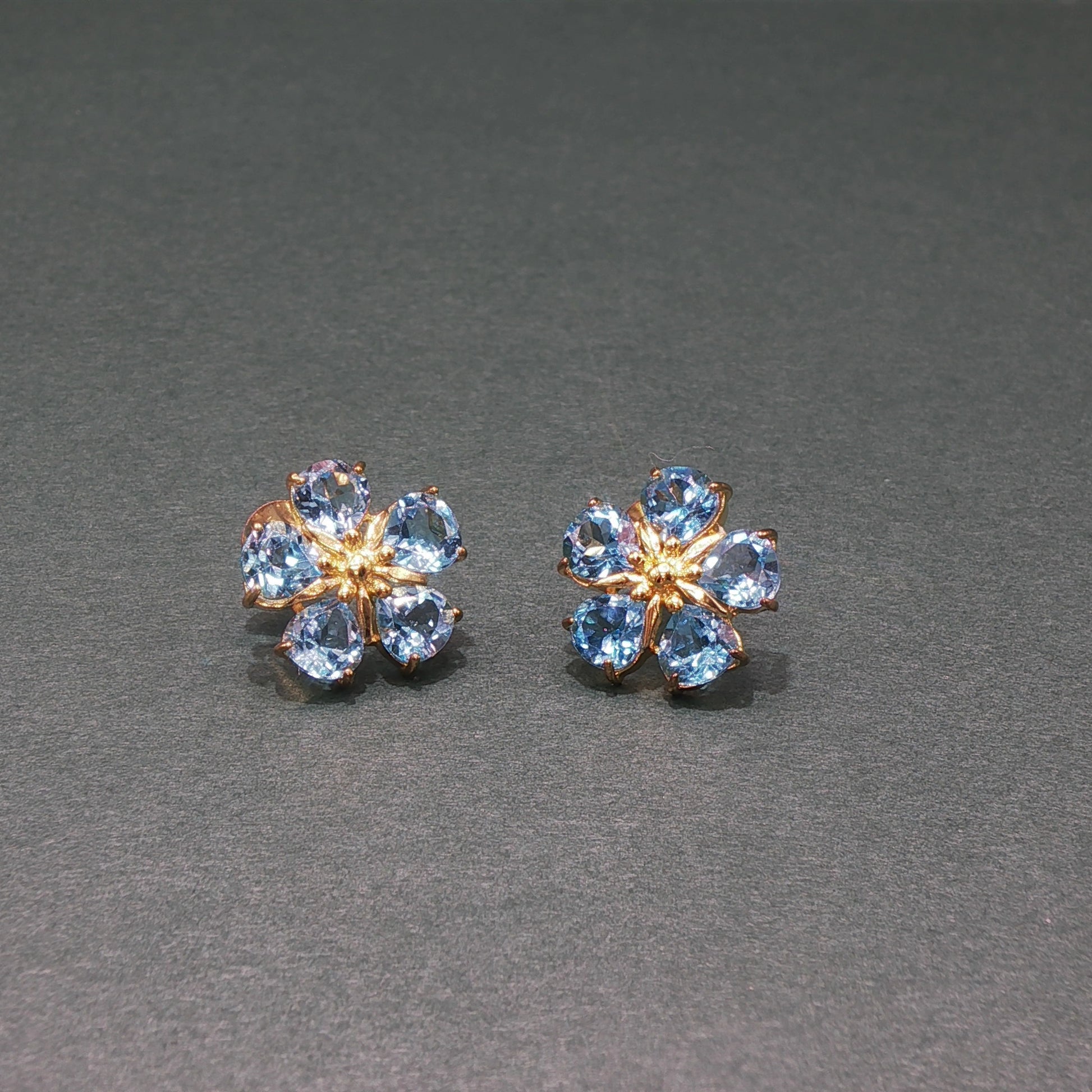 Pair of flower-shaped earrings with blue gemstones on a gray background