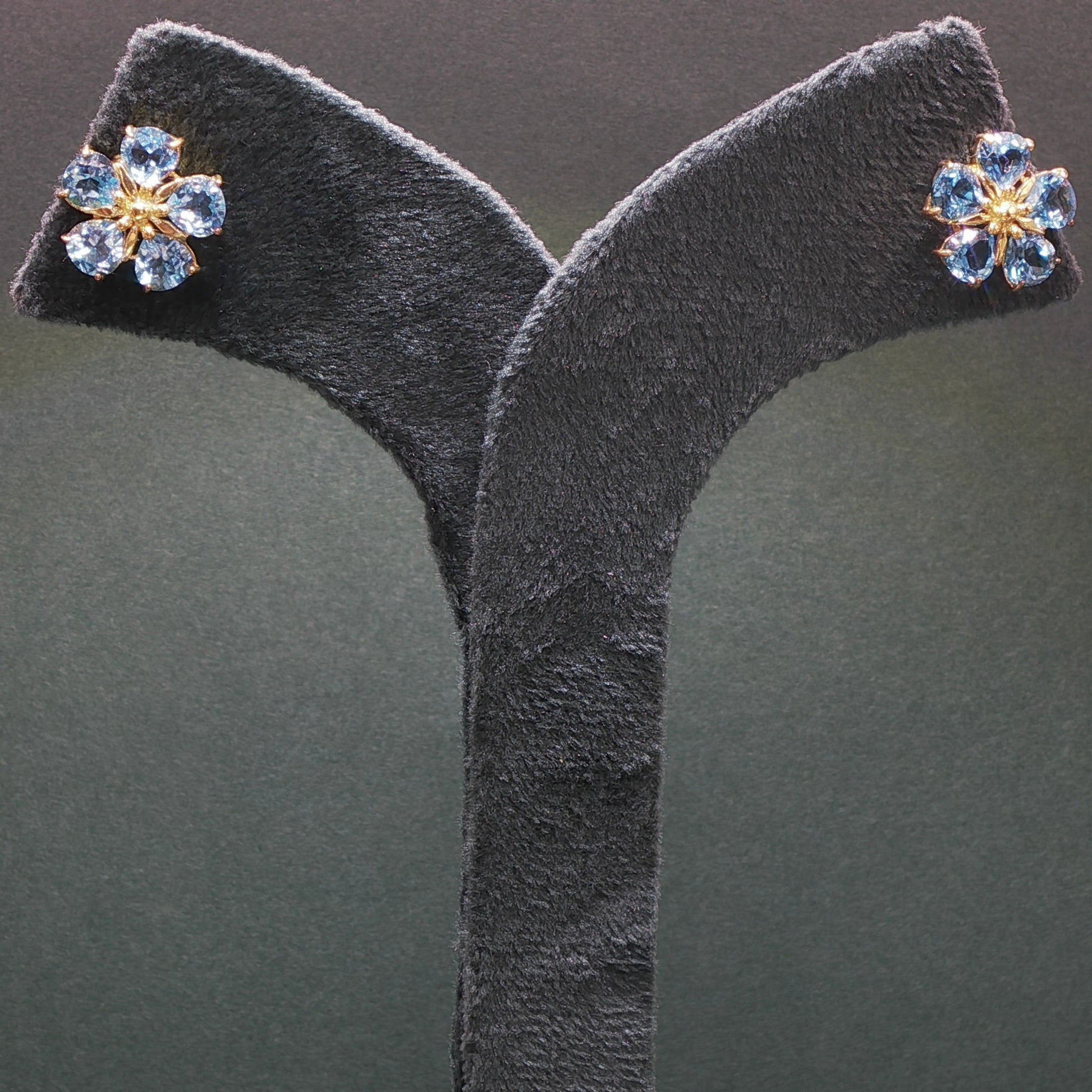 Pair of earrings with blue gemstones on a gray stand against a dark background