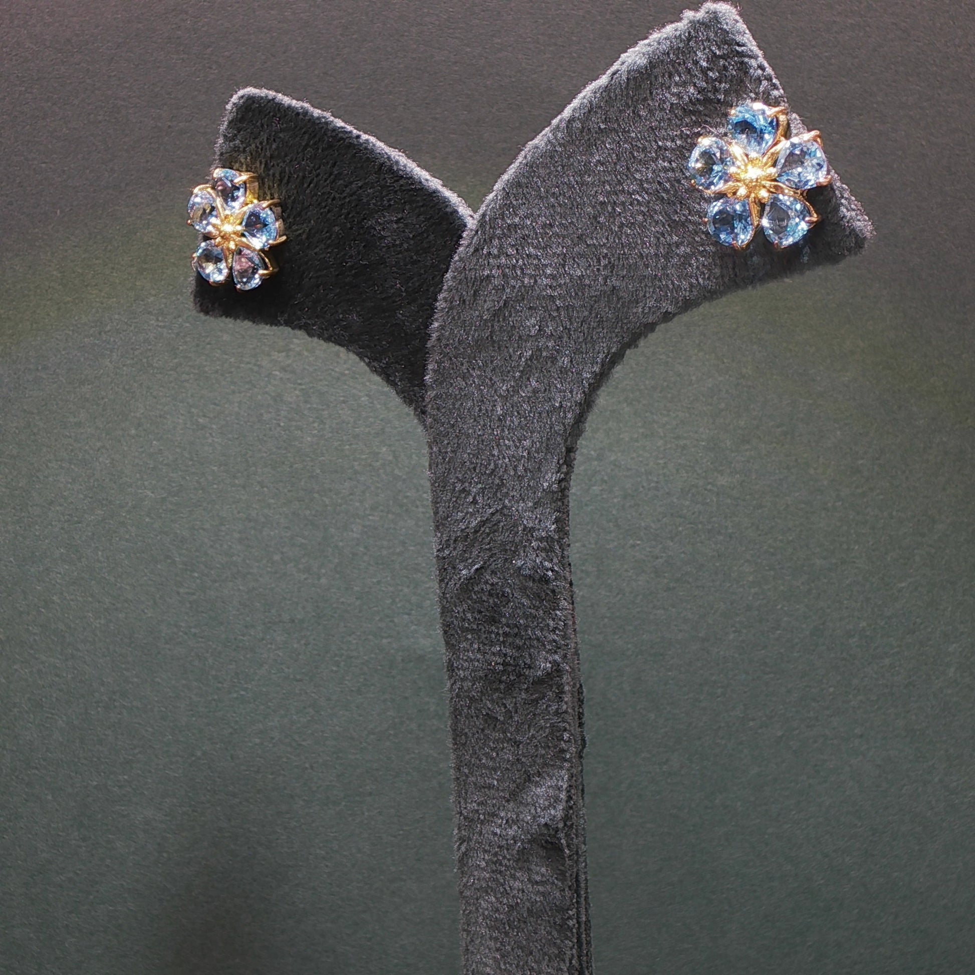 Pair of floral earrings with gemstones on a gray stand against a dark background