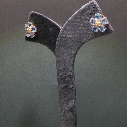 Pair of floral earrings with gemstones on a gray stand against a dark background