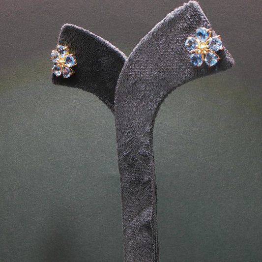 Pair of floral earrings with gemstones on a gray stand against a dark background