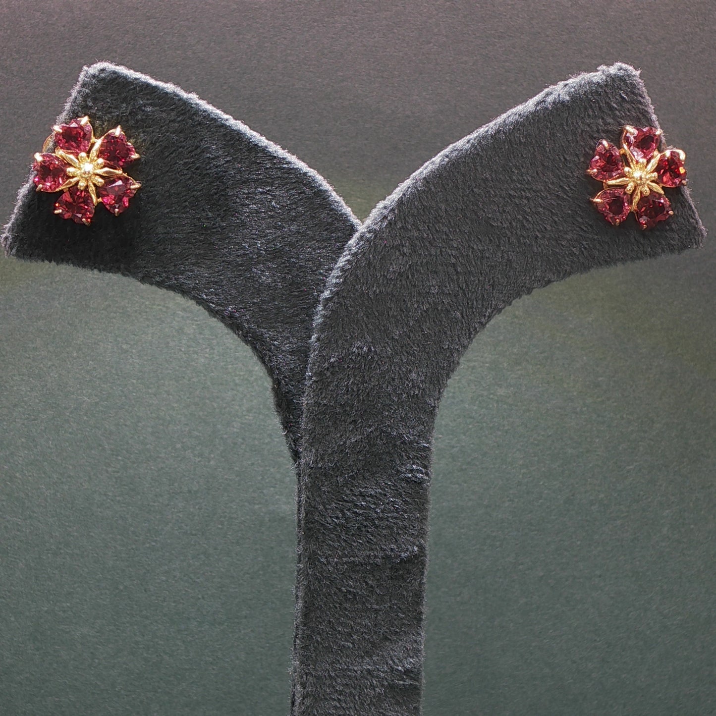 Floral earrings with red gemstones on a gray stand against a dark background