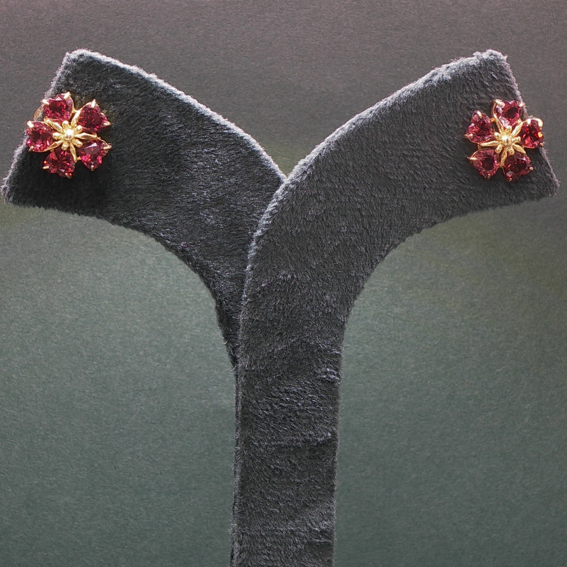 Floral earrings with red gemstones on a gray stand against a dark background