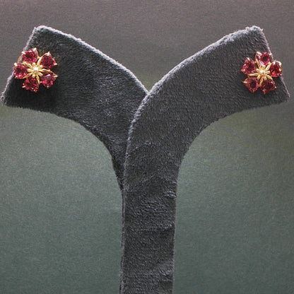 Floral earrings with red gemstones on a gray stand against a dark background