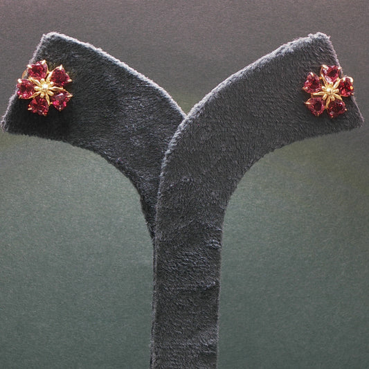 Floral earrings with red gemstones on a gray stand against a dark background