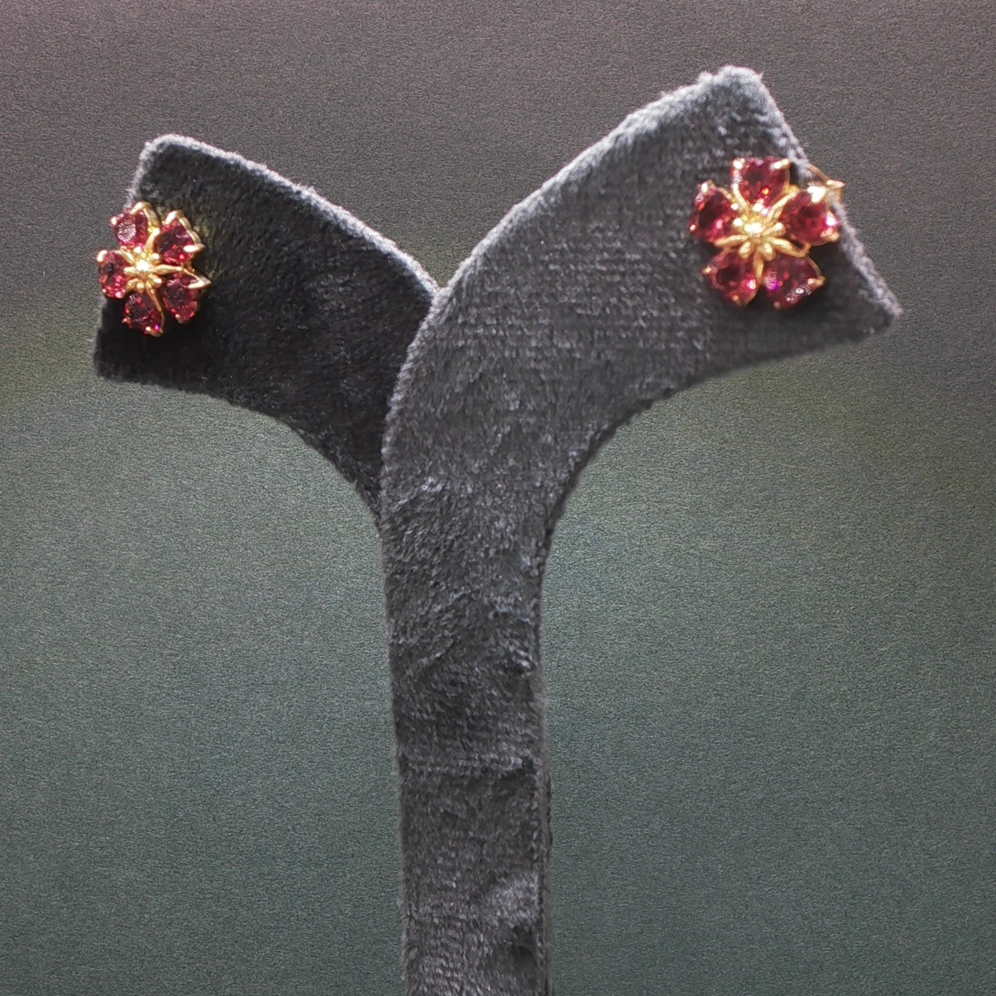 Pair of earrings with red gemstones on a gray stand against a dark background