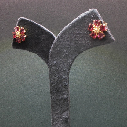 Pair of earrings with red gemstones on a gray stand against a dark background