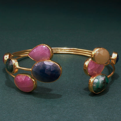 Gold bracelet with colorful gemstones on a dark green background

