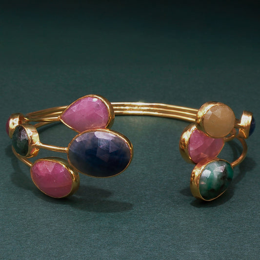 Gold bracelet with colorful gemstones on a dark green background

