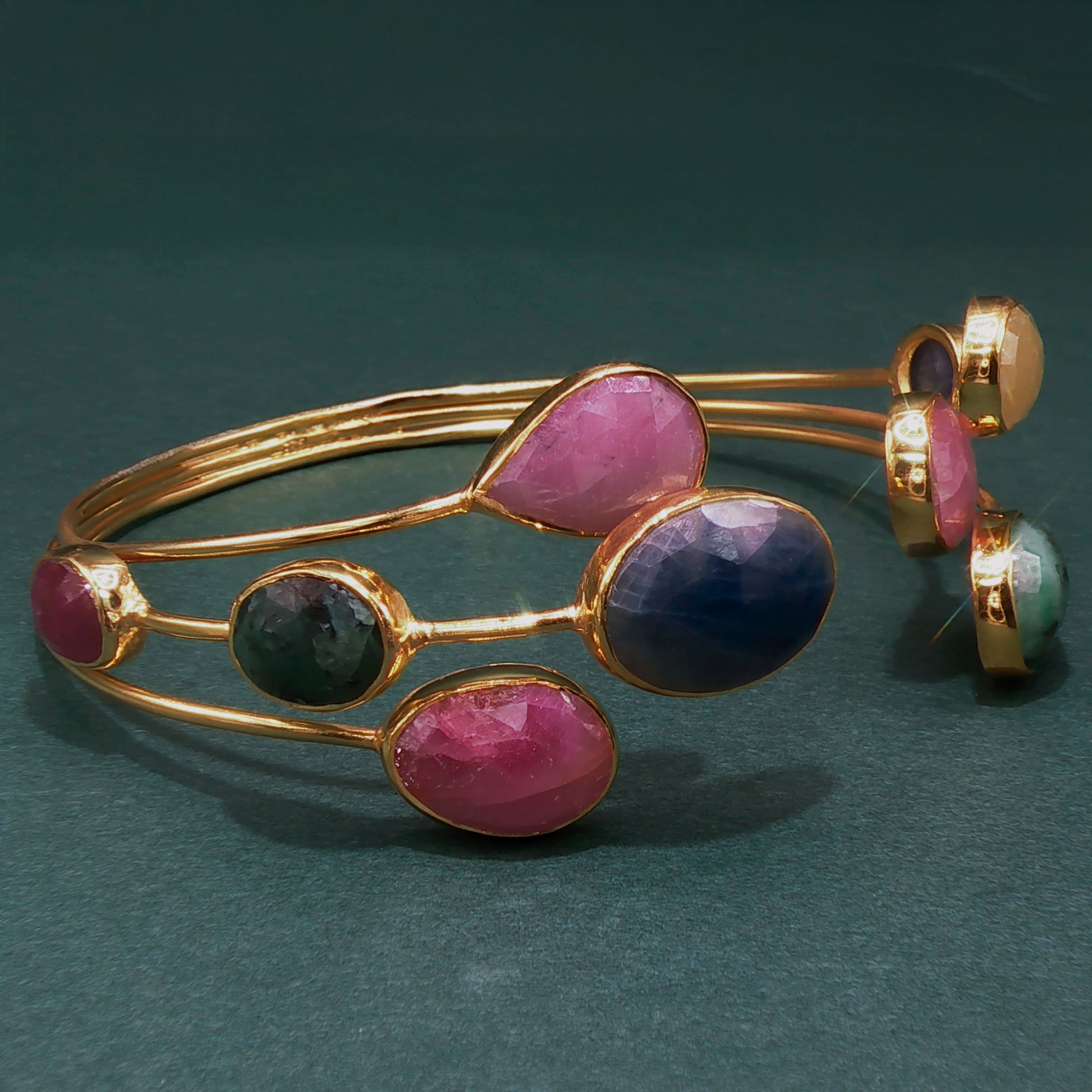 Gold bracelet with pink and purple stones on a dark green background

