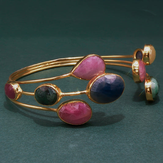 Gold bracelet with pink and purple stones on a dark green background

