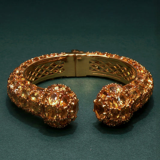 Gold bracelet with intricate design and large gemstones on a dark green background