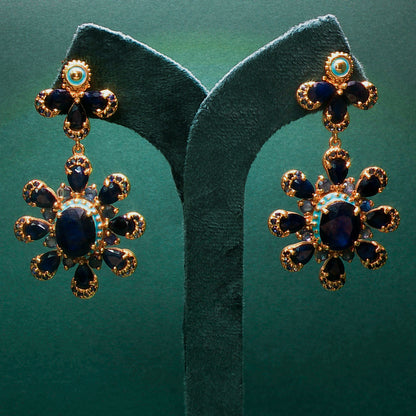 Pair of gold and blue gemstone earrings on a green stand.