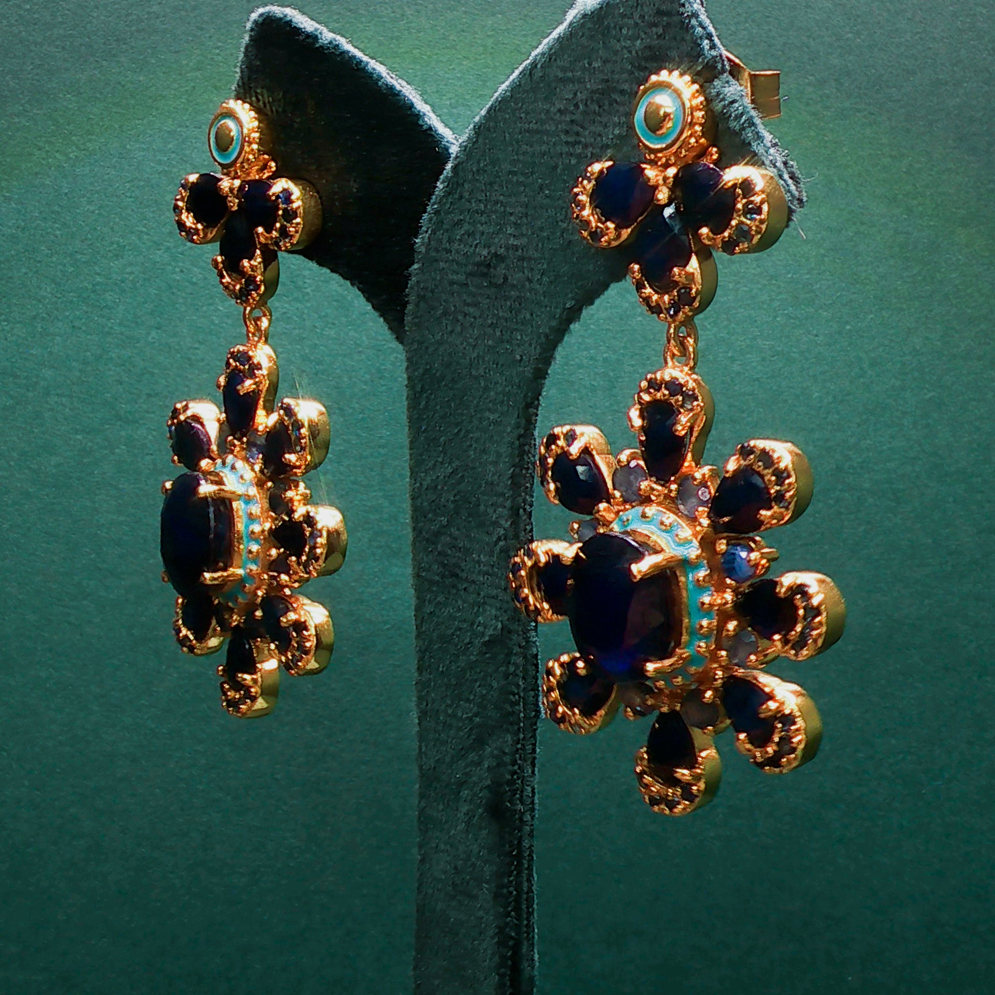Gold and blue earrings on a green stand with a green background