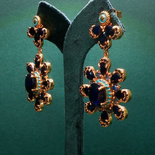 Gold and blue earrings on a green stand with a green background