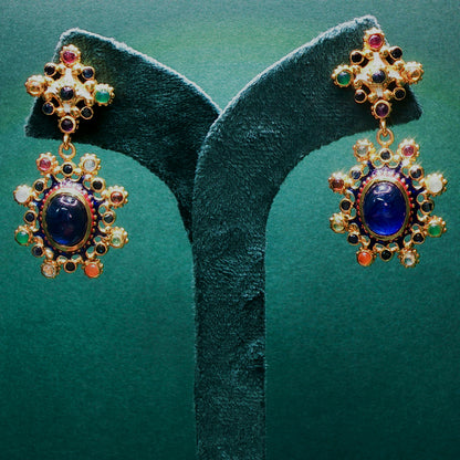 Ornate earrings with blue gemstones on a green velvet stand