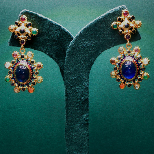 Ornate earrings with blue gemstones on a green velvet stand