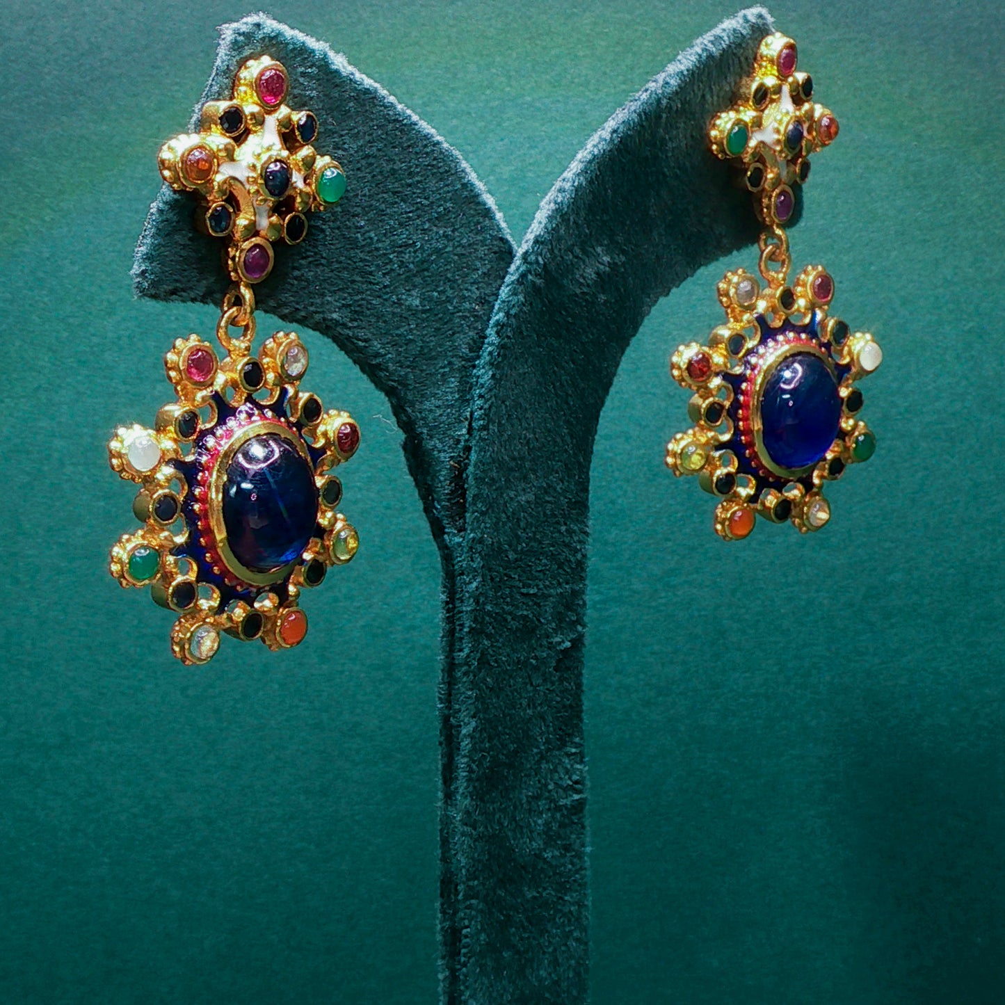 Colorful gemstone earrings on a green stand against a teal background