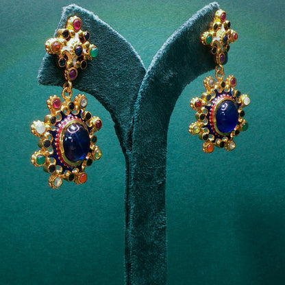 Colorful gemstone earrings on a green stand against a teal background