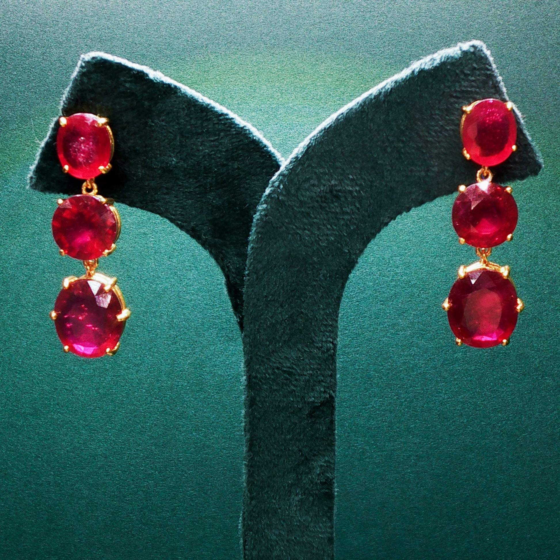 Red gemstone earrings on a green stand