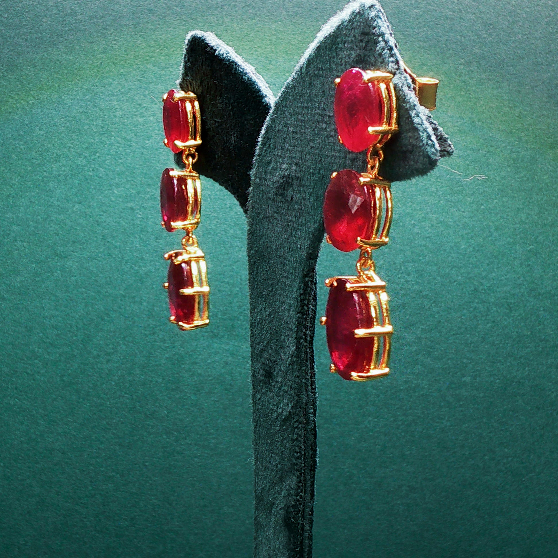 Gold earrings with red gemstones on a green stand