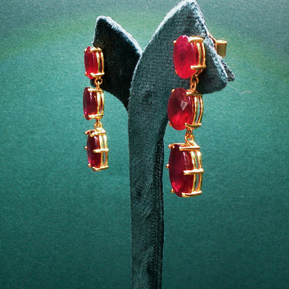 Gold earrings with red gemstones on a green stand