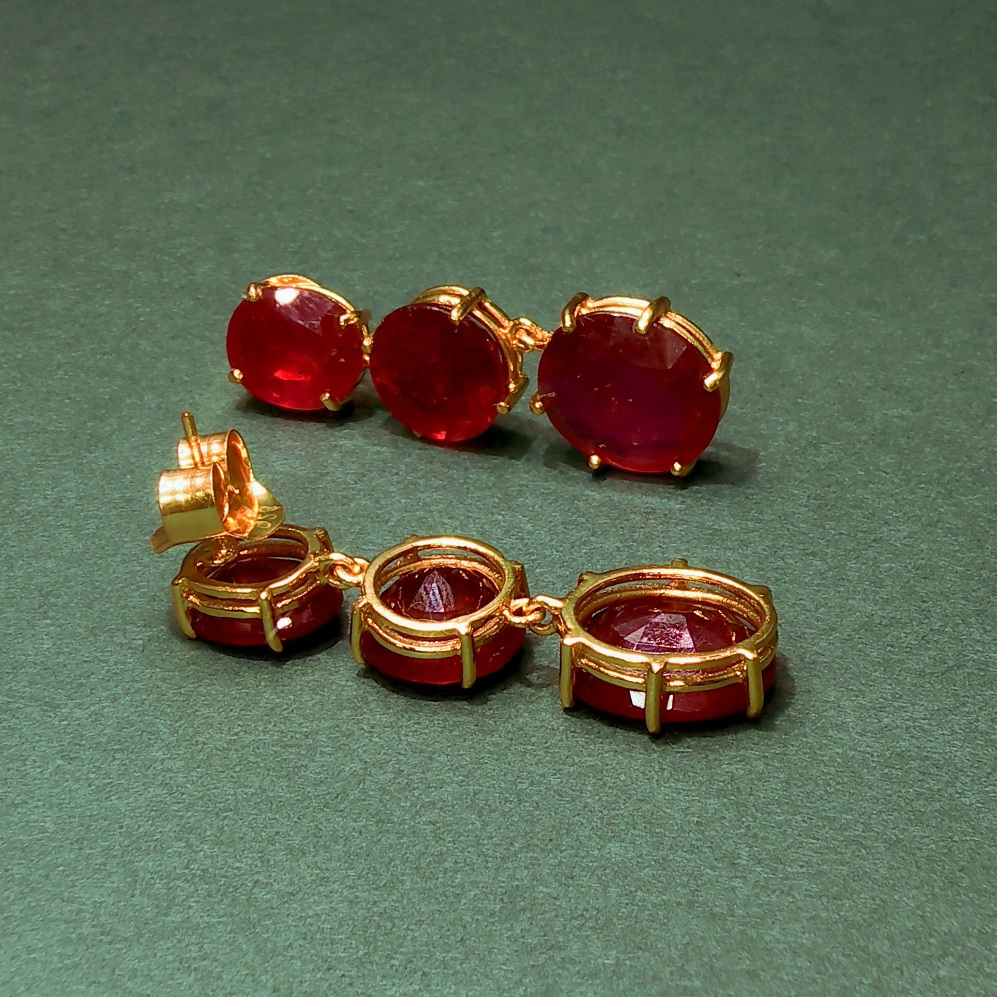 Pair of gold earrings with red gemstones on a green background