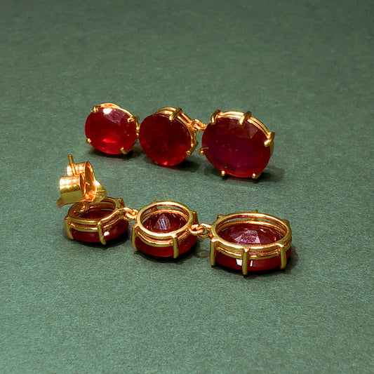 Pair of gold earrings with red gemstones on a green background