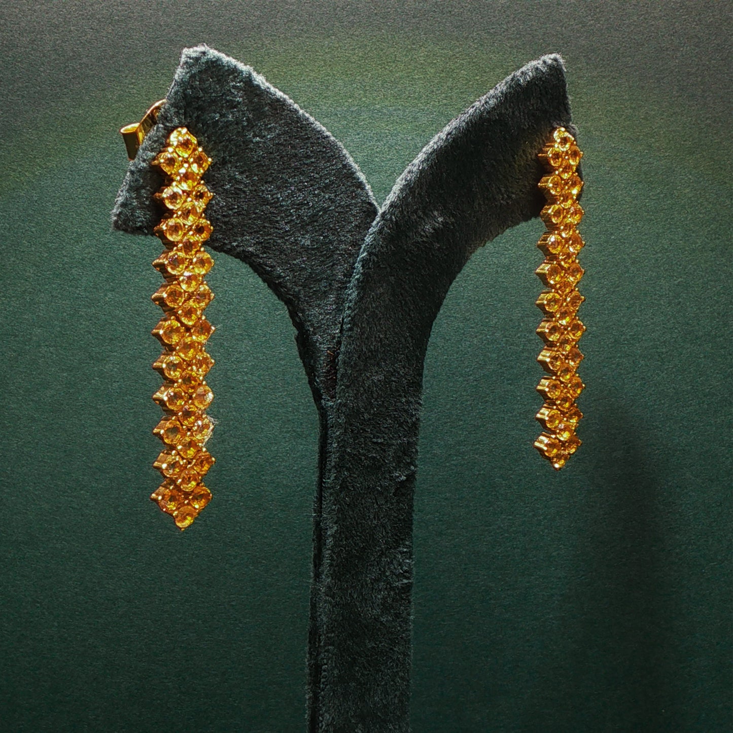 Pair of gold earrings on a dark green stand against a matching background