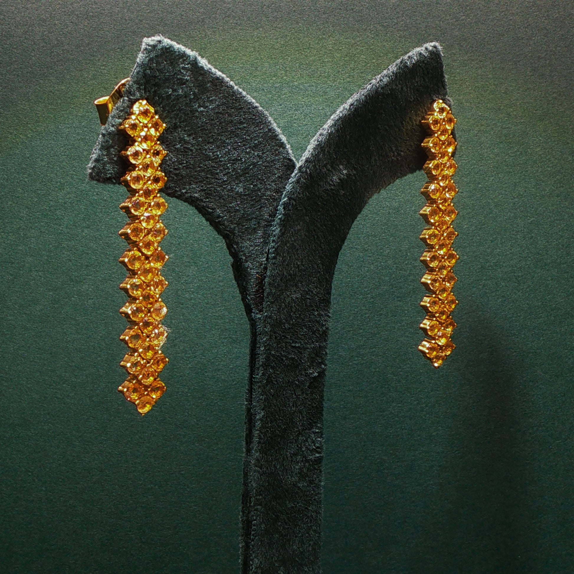 Pair of gold earrings on a dark green stand against a matching background