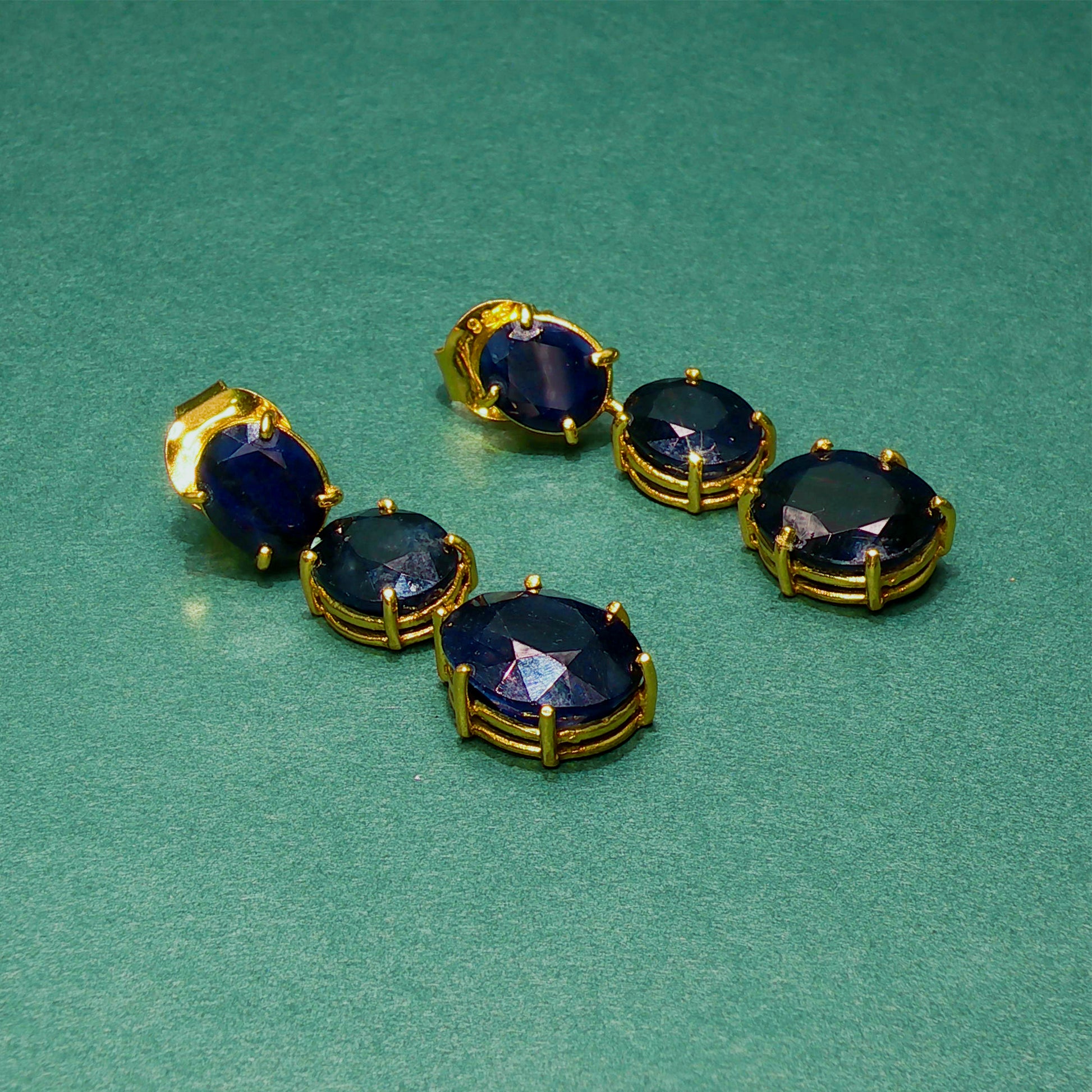 Set of gold and blue gemstone earrings on a green background