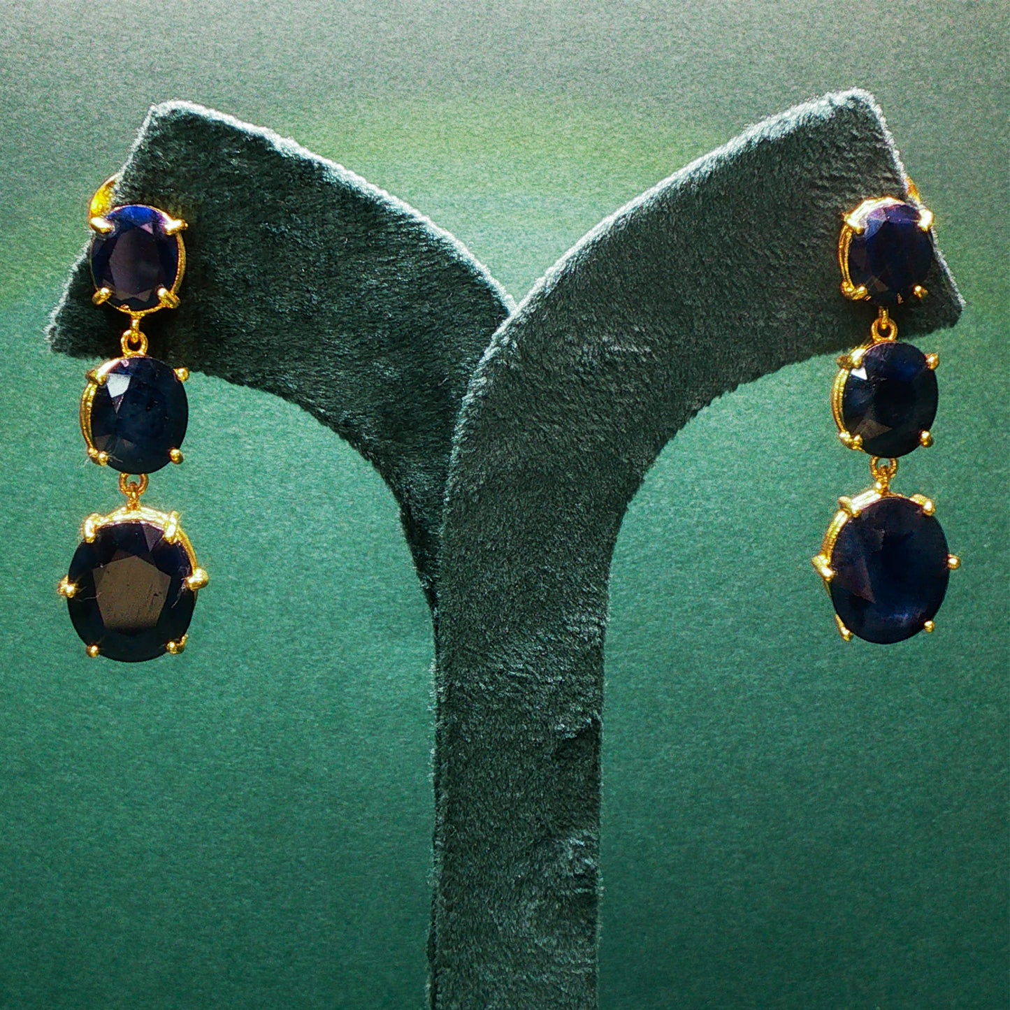 Pair of gold earrings with dark gemstones on a green stand.