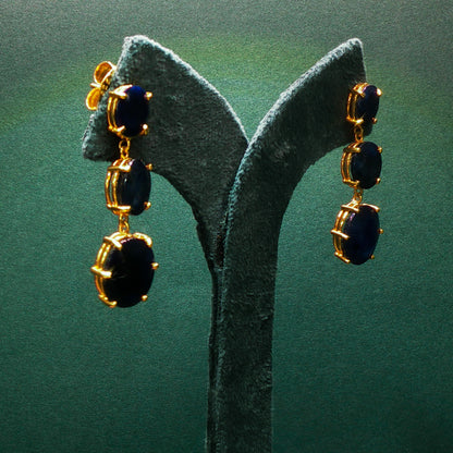 Gold earrings with black stones on a green stand
