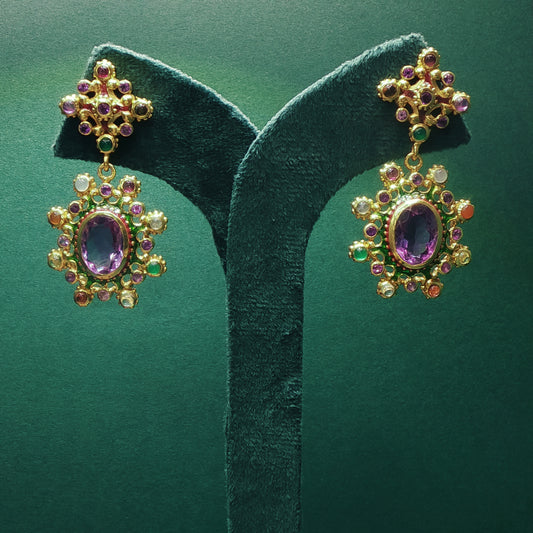Ornate gold earrings with gemstones on a green velvet stand