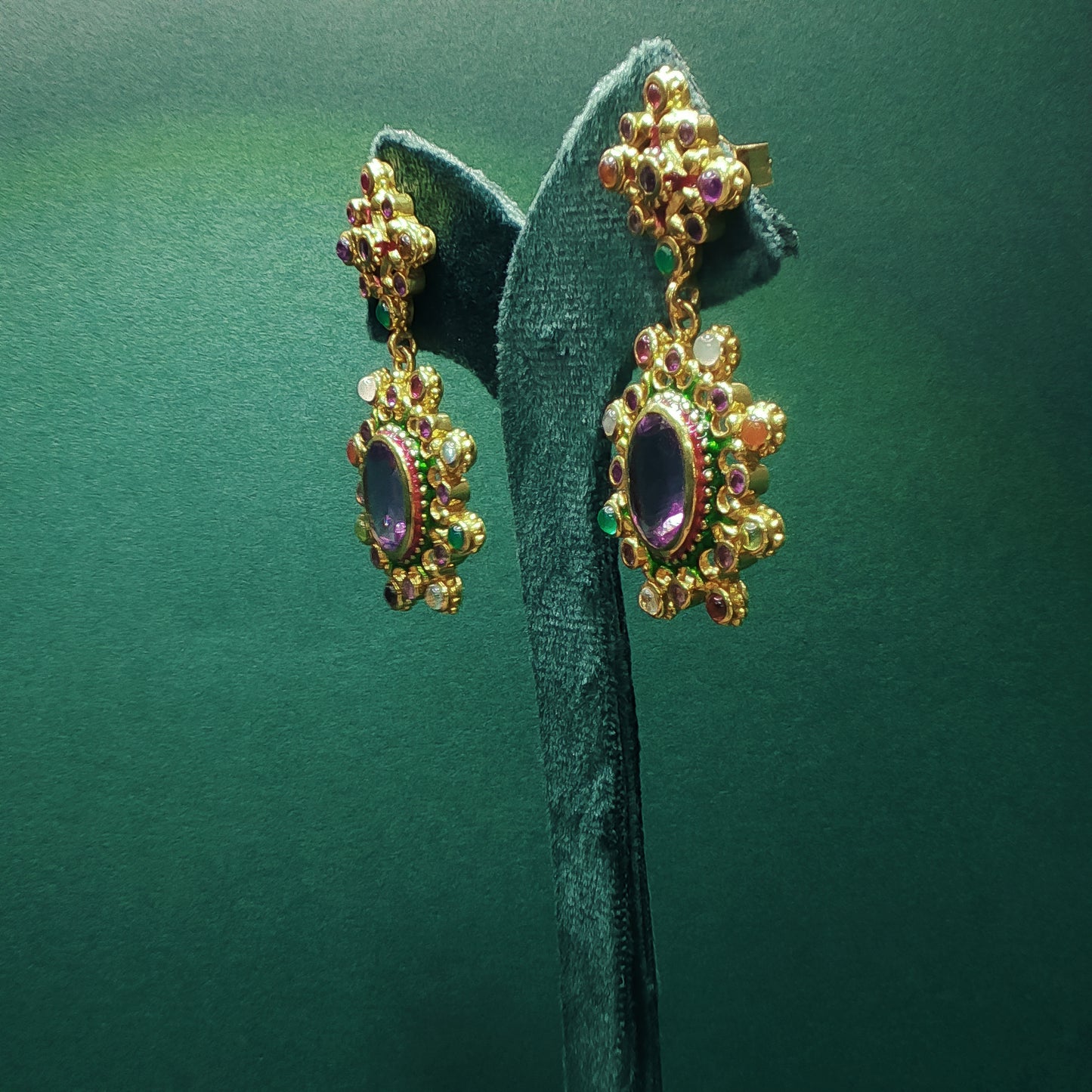 Gold earrings with gemstones on a green stand against a green background

