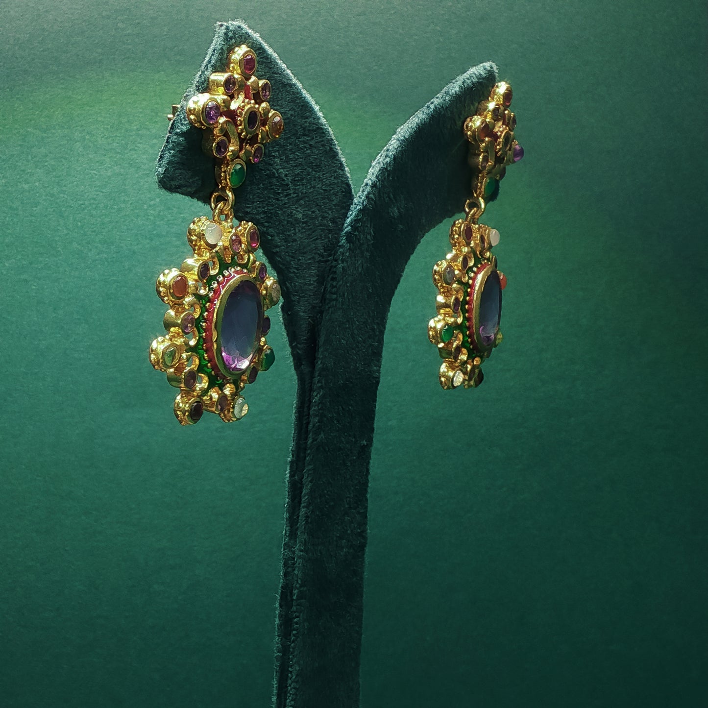 Gold earrings with gemstones on a green stand against a green background


