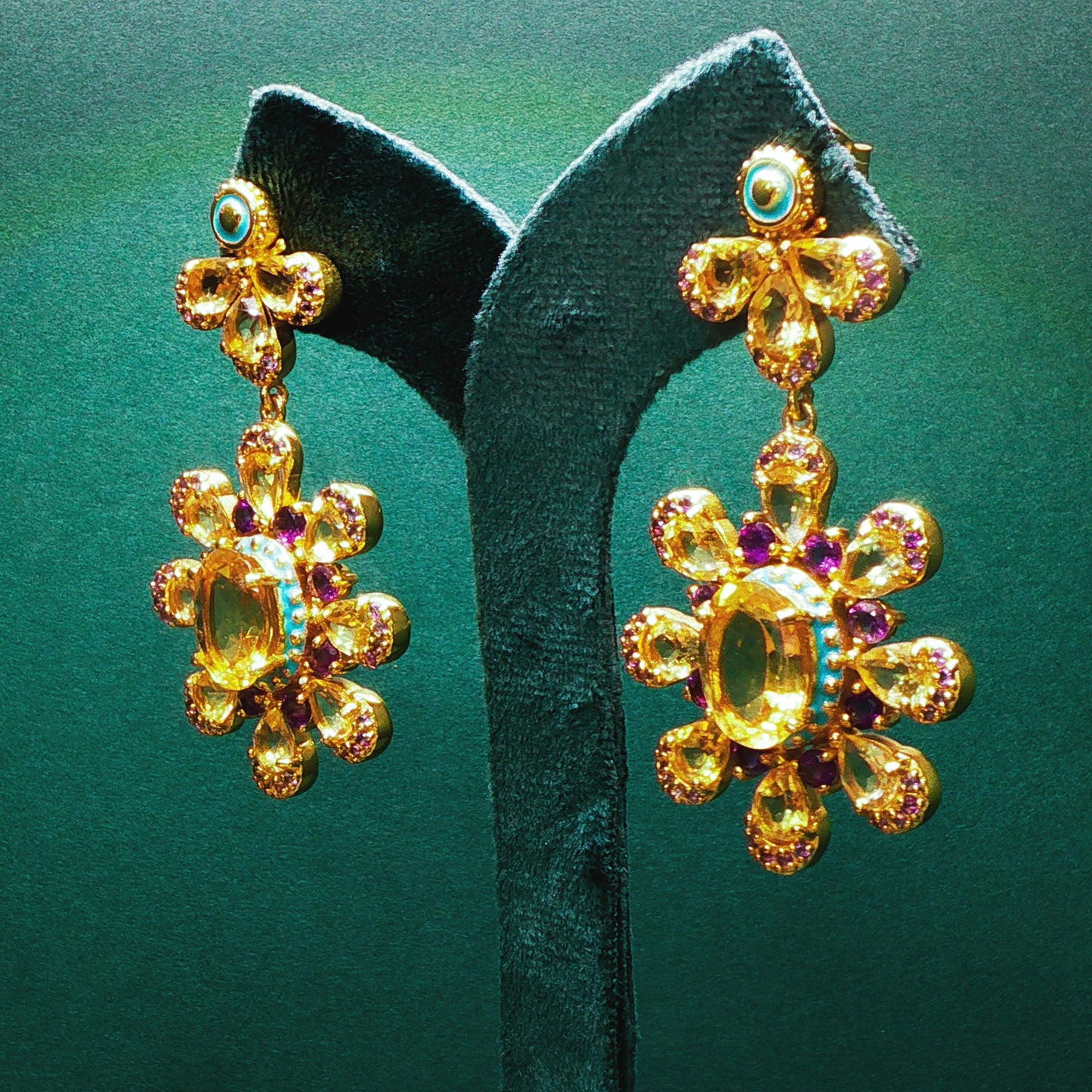 Gold earrings with gemstones on a green stand