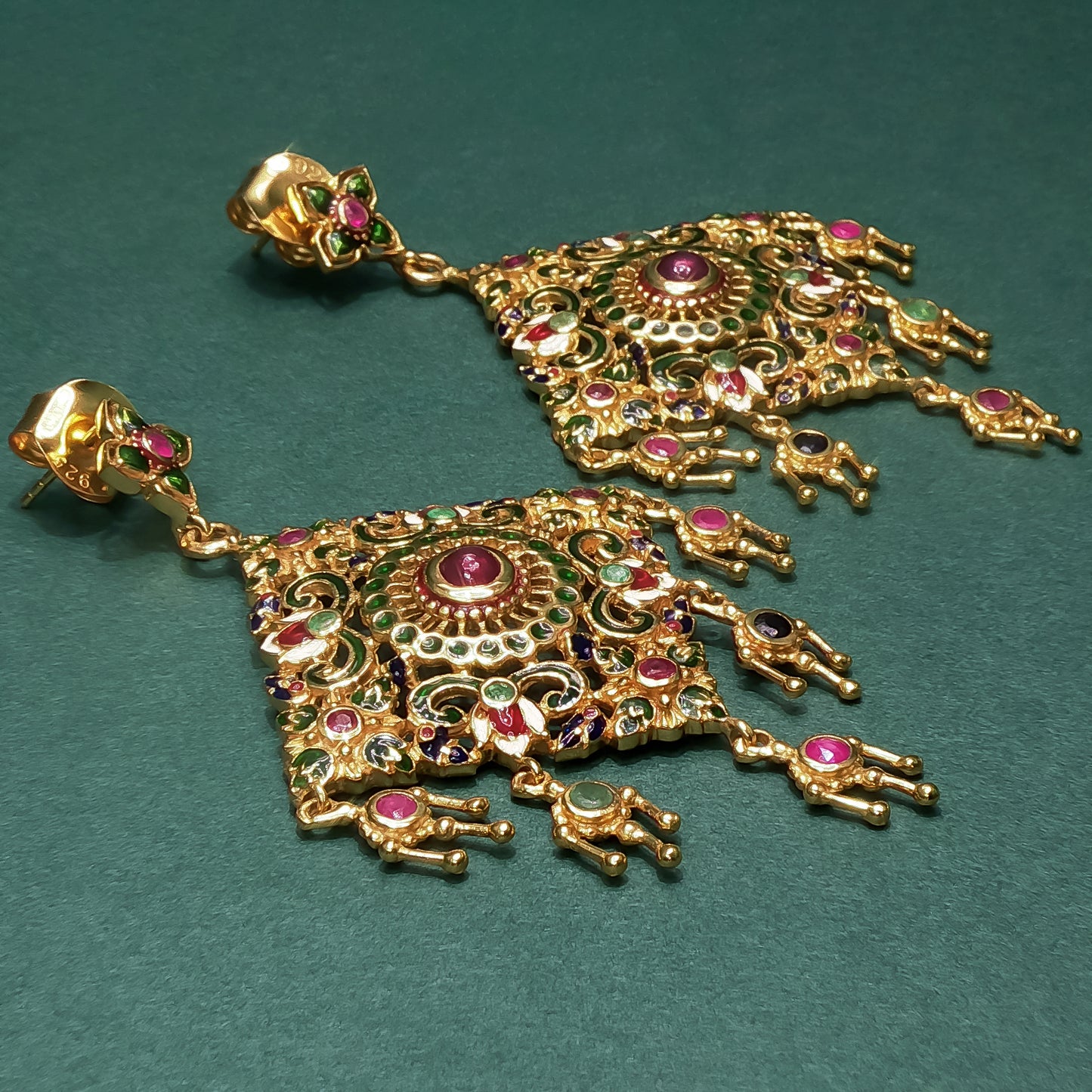 Gold earrings with intricate designs and gemstones on a green background

