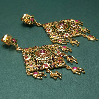 Gold earrings with intricate designs and gemstones on a green background

