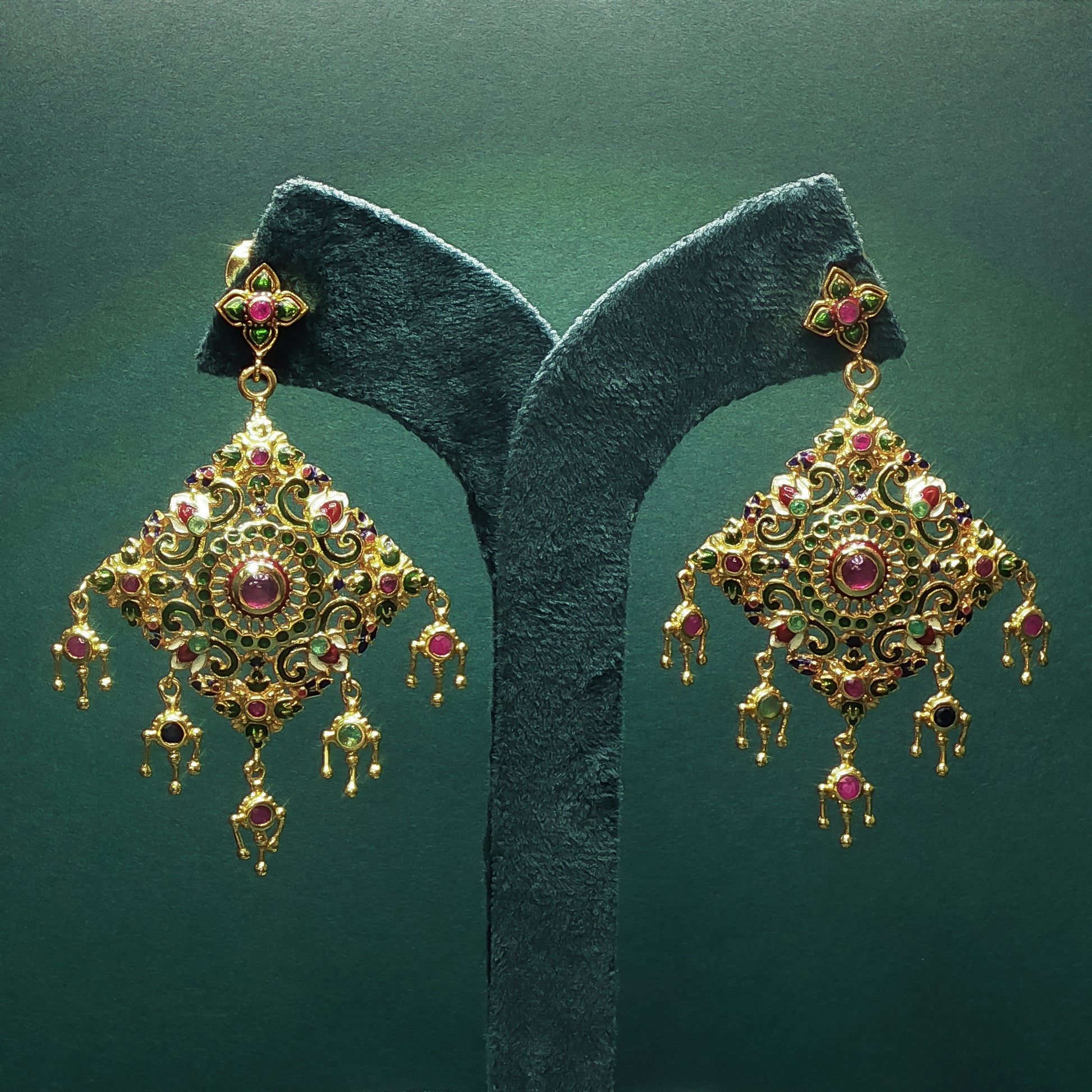 Gold earrings with red gemstones on a green stand against a green background

