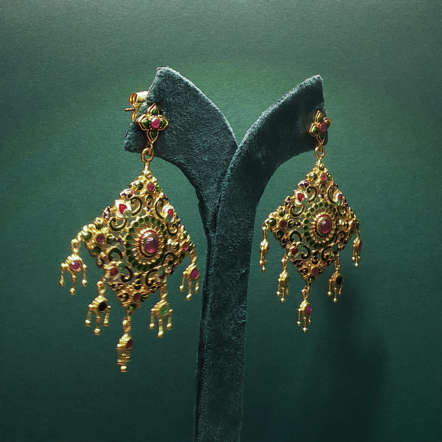 Gold earrings with red gemstones on a green stand against a green background

